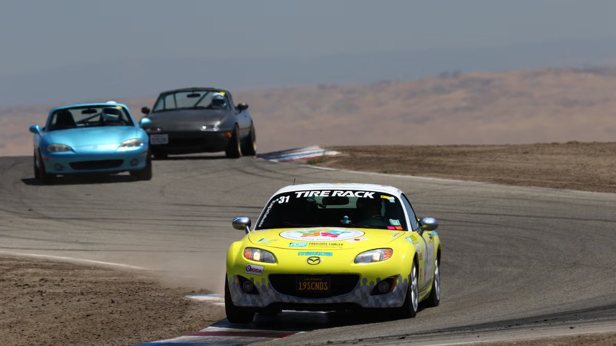 Mazda Miata sports cars racing on a sunny day at Buttonwillow Raceway, California.